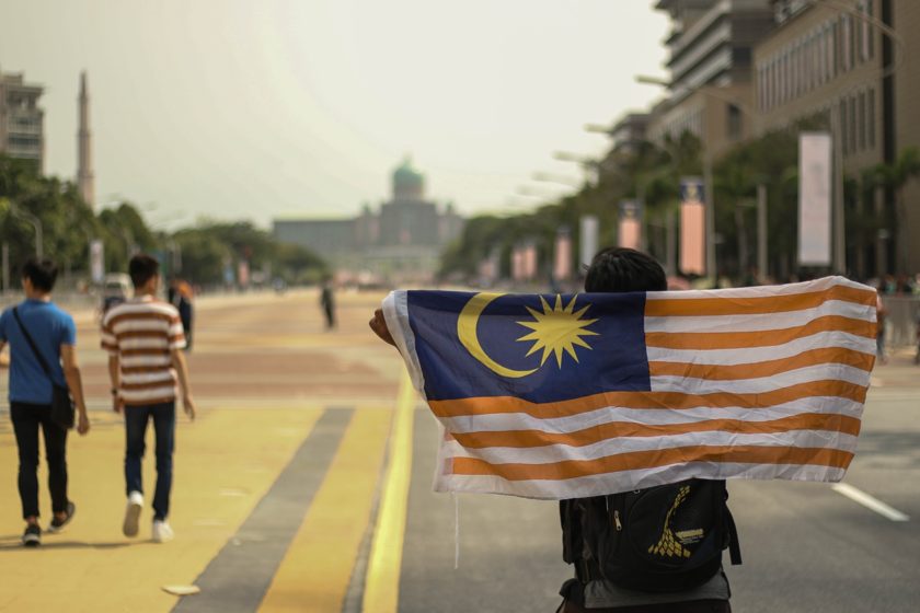Person holding a Malaysian flag across their shoulders on a city street