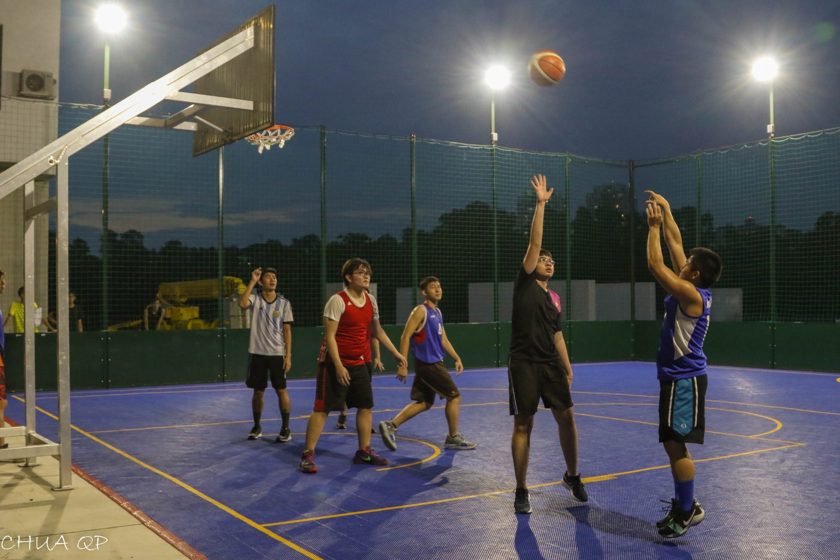 Basketball players reaching for the ball on an outdoor court at night