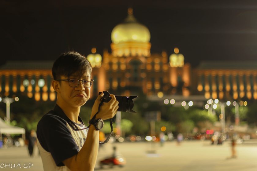 Photographer holding a camera in front of an illuminated building at night