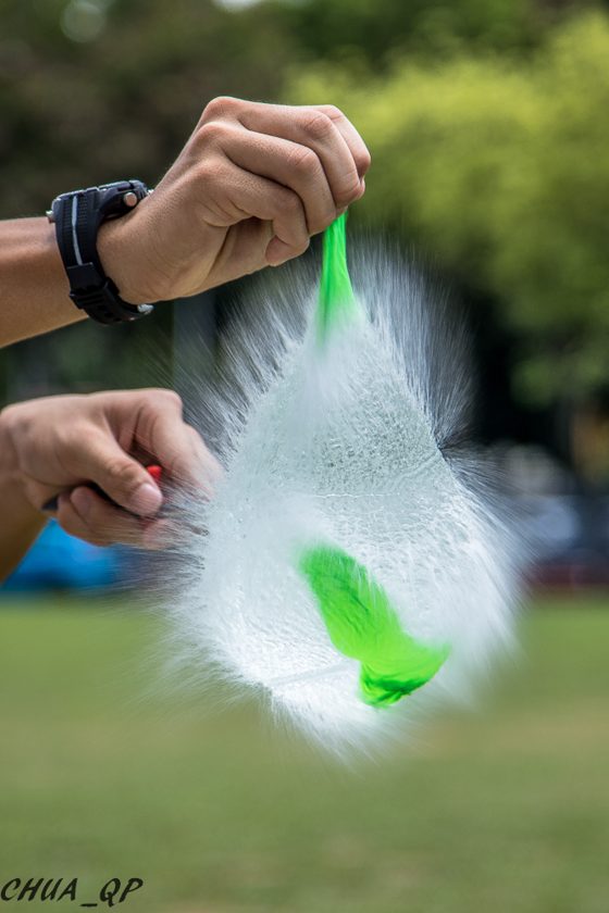 A green balloon bursting in a spray of water
