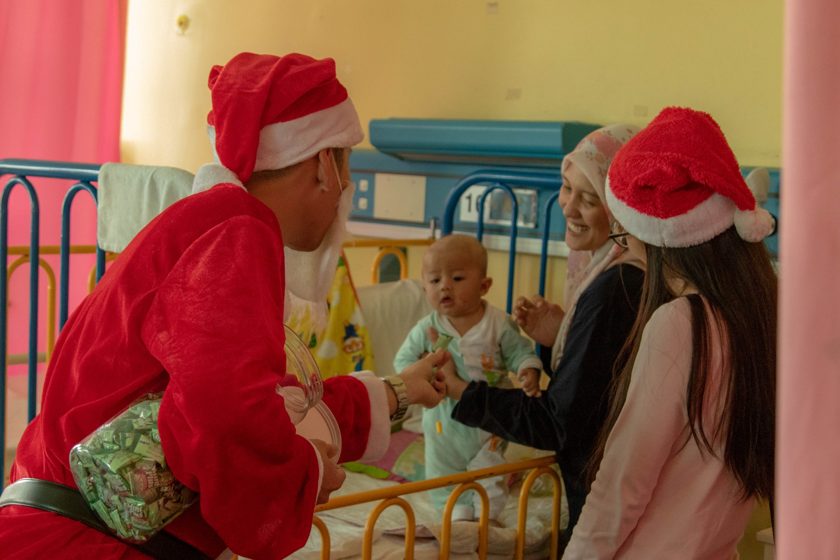 People wearing Santa hats visiting a child beside a cot