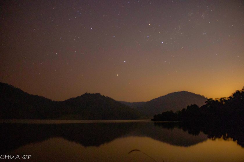 Stars above dark hills reflected in still water