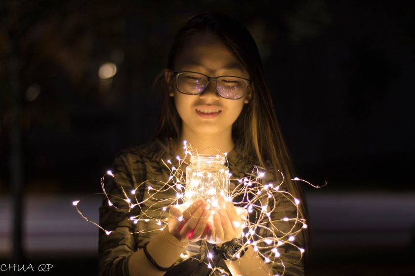 Portrait of a person holding warm string lights at night
